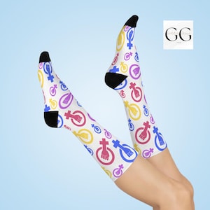 May include: A pair of white knee-high socks with a pattern of pink, blue, and yellow female symbols and fists. The socks are worn on a person's legs.
