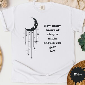 May include: White t-shirt with a black crescent moon and star graphic. The text reads, "How many hours of sleep a night should you get? 6-7". The shirt is made of a soft material.
