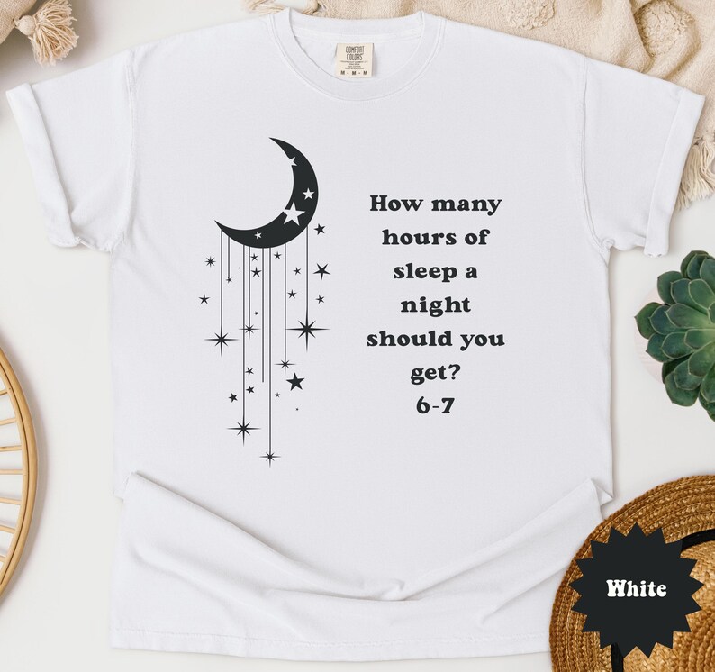 May include: White t-shirt with a black crescent moon and star graphic. The text reads, "How many hours of sleep a night should you get? 6-7". The shirt is made of a soft material.