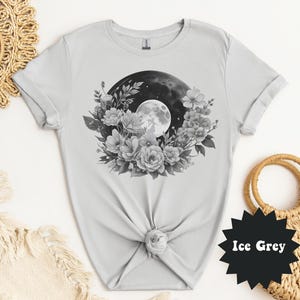 May include: Ice grey t-shirt featuring a black and white floral and moon graphic. The design includes a full moon, surrounded by flowers and foliage. The shirt is made of a soft material.