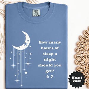 May include: A blue Comfort Colors t-shirt with a white crescent moon and stars design. The shirt features the text "How many hours of sleep a night should you get? 6-7". The shirt is size XL-TG-EG.