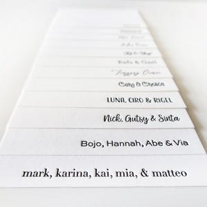 May include: A stack of white cards with black text listing names. The names include "mark, karina, kai, mia, & matteo", "Bojo, Hannah, Abe & Via", "Nick. Gutsy & Sinta", "LUNA, CIRO & RIGEL", "Carg & Chesca", "Terry Owen", "Rala & G", "Spy C", and more.