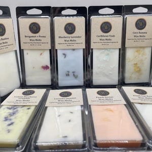 May include: A collection of rectangular wax melts in clear plastic packaging with tan labels. Each label displays a scent name, such as Lemon Verbena, Blueberry Lavender, or Peach Nectar, and states a net weight of 2 oz for the organic soy wax.