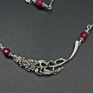 May include: A silver necklace with a floral design and red gemstone beads.