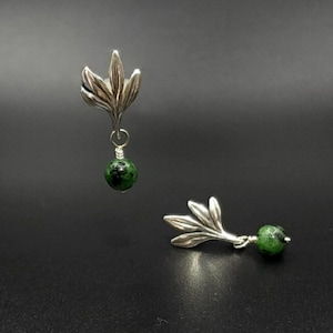 May include: A pair of silver earrings with green gemstone drops. Each earring features a delicate silver leaf design.
