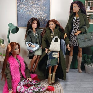 Könnte beinhalten: Vier Modepuppen posieren in einer Raumkulisse. Die Puppen tragen verschiedene Outfits, darunter Mäntel, Kleider und gemusterte Hosen. Zu den Accessoires gehören Handtaschen und Schmuck. Die Farbpalette umfasst Grün-, Rosa- und Neutraltöne.