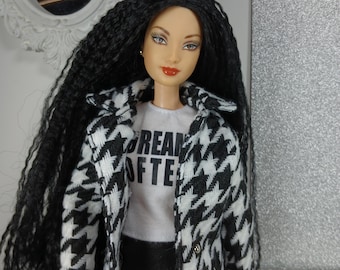 May include: A doll with long black hair, wearing a black and white houndstooth coat over a white t-shirt with the text "DREAM OFTEN". The doll is also wearing a black skirt. The background includes a white framed mirror and a textured wall.