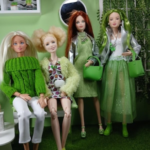 Peut inclure: Quatre poupées de mode portant des tenues et des accessoires verts. Les poupées sont debout devant un fond vert.