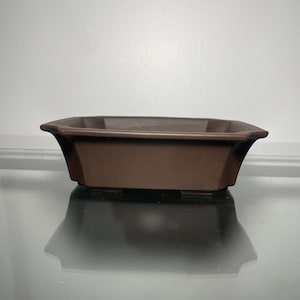 May include: A brown rectangular ceramic bonsai pot with four small feet.