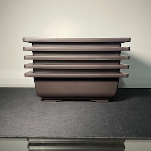 May include: A stack of five brown plastic square plant pots. The pots are stacked on a black surface.