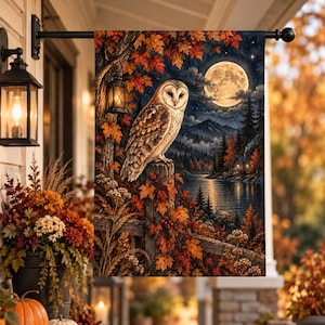 May include: A rectangular garden flag featuring a barn owl perched on a wooden fence post amidst autumn foliage. The scene includes a full moon, a starry night sky, a lake, and a small cabin. A hanging lantern is attached to a nearby tree.