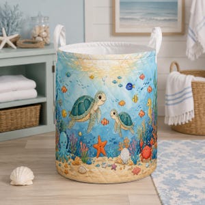 May include: A cylindrical quilted laundry hamper featuring a colorful underwater scene with two sea turtles, an octopus, a crab, a seahorse, starfish, and various tropical fish swimming among coral and seashells on a sandy ocean floor.
