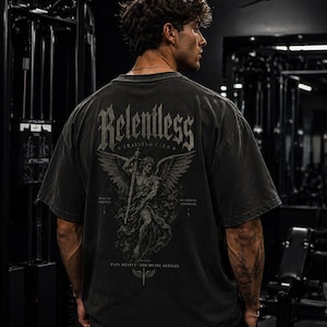 May include: A charcoal gray oversized t-shirt featuring a large back graphic of a winged figure holding a sword. The text reads Relentless Training Club, Built in Silence, Defined by Discipline, and Pain Shapes Discipline Defines.