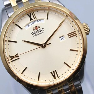 May include: A gold and silver-toned Orient automatic wristwatch with a cream-colored face. The watch features Roman numeral hour markers, a day and date display, and gold hands. The watch band is a combination of gold and silver links.