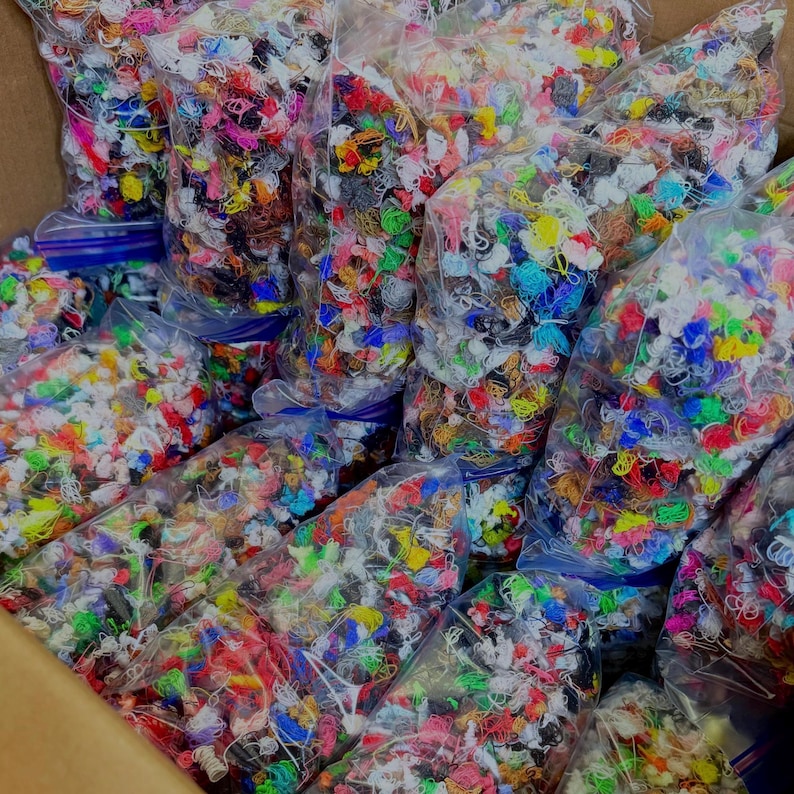 May include: Multiple clear plastic bags filled with a large assortment of small, tangled, multi-colored thread scraps. The collection includes various vibrant hues such as red, blue, green, yellow, pink, and white, all packed together in a box.
