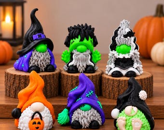 May include: A collection of six Halloween-themed gnome figurines. The top row features a witch gnome, a green monster gnome, and a bride gnome. The bottom row includes an orange hat gnome with a pumpkin bucket, a purple hat gnome, and a black hat gnome.