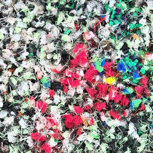 May include: A dense, tangled collection of thin, multi-colored plastic filament strands. The chaotic pile features a vibrant mix of red, black, white, lime green, blue, and yellow loops and messy threads, creating a textured, abstract surface.