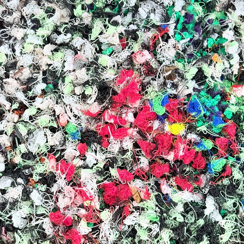 May include: A dense, tangled collection of thin, multi-colored plastic filament strands. The chaotic pile features a vibrant mix of red, black, white, lime green, blue, and yellow loops and messy threads, creating a textured, abstract surface.