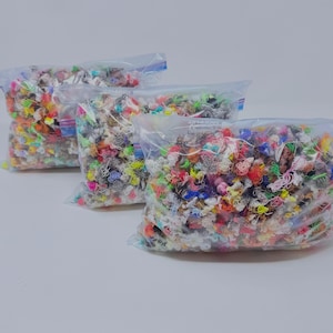 May include: Three clear plastic resealable bags filled with a dense collection of small, tangled, multi-colored thread scraps. The assortment includes various vibrant hues such as neon yellow, bright pink, blue, orange, and white, all packed together.