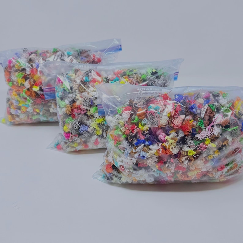 May include: Three clear plastic resealable bags filled with a dense collection of small, tangled, multi-colored thread scraps. The assortment includes various vibrant hues such as neon yellow, bright pink, blue, orange, and white, all packed together.