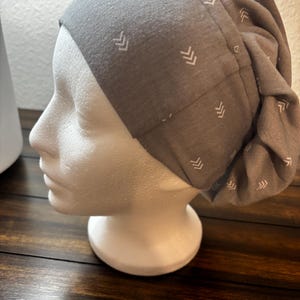 Op de afbeelding: Grijze katoenen beanie met een wit chevron-patroon. De beanie is bovenaan gevouwen en heeft een losse pasvorm.