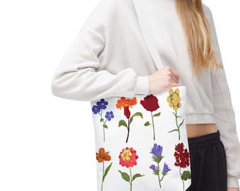May include: A white canvas tote bag with a colorful floral print. The flowers are red, orange, yellow, blue, and green. The bag has two straps and is perfect for carrying groceries or other items.