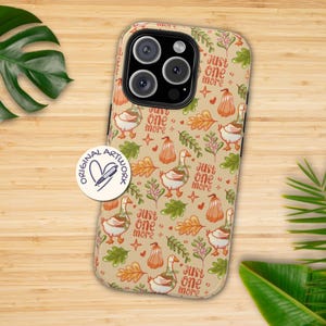 May include: A beige phone case featuring a repeating pattern of geese, pumpkins, leaves, and the text "Just one more." The case has a glossy finish and a camera cutout. The design includes orange, green, and brown elements.