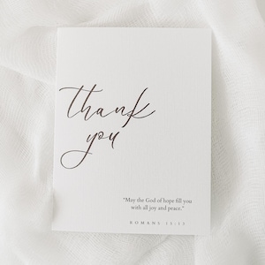May include: A white card with the words "Thank you" written in elegant cursive script. Below the greeting is a quote from Romans 15:13, "May the God of hope fill you with all joy and peace."
