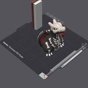 Może przedstawiać: Cyfrowy model 3D stworzenia z czarnym ciałem, białymi oznaczeniami przypominającymi kości i czerwonym wnętrzem skrzydeł, umieszczony na płycie Bambu Textured PEI. Obok znajduje się wysoki, prostokątny filar z czerwonymi, czarnymi i białymi pionowymi pasami.