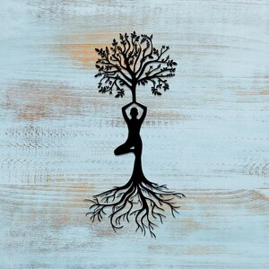 May include: A black silhouette of a person in a yoga pose with a tree growing out of their head and roots extending down from their feet. The background is a light blue wooden surface.