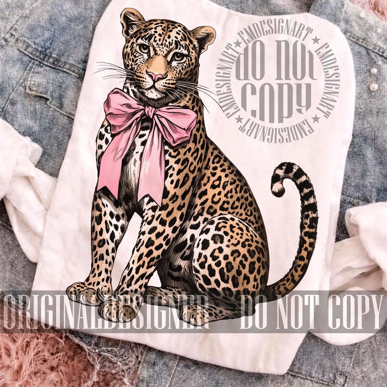 May include: White t-shirt featuring a detailed illustration of a leopard with a pink bow. The leopard has a spotted coat and is sitting upright. The text "DO NOT COPY" is printed on the shirt.