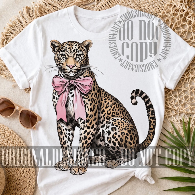 May include: White t-shirt featuring a detailed illustration of a leopard with a pink bow. The leopard has a spotted coat and is sitting upright. The text "ORIGINAL DESIGN" and "DO NOT COPY" are visible.