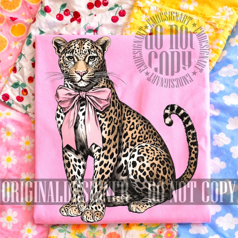 May include: A pink t-shirt featuring a detailed illustration of a leopard wearing a pink bow. The leopard has a spotted coat and is sitting upright. The text "ORIGINAL DESIGNER" and "DO NOT COPY" are printed on the shirt.