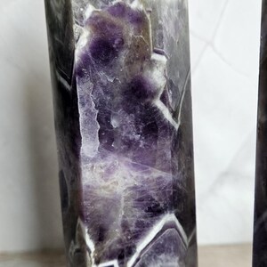 K&ouml;nnte beinhalten: Ein hoher, facettierter Amethyst-Kristallpunkt mit polierter Oberfl&auml;che. Der Kristall weist eine Mischung aus violetten, wei&szlig;en und grauen Farbt&ouml;nen mit sichtbaren inneren Mustern auf. Der Kristall ist ein dekorativer Gegenstand.
