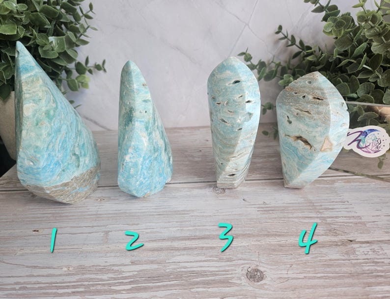 May include: Four blue and tan gemstone sculptures with varying shapes and textures. The gemstones are numbered 1 through 4 with teal-colored numbers. The background includes greenery and a light-colored surface.