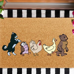 May include: A rectangular doormat with a light brown background features a line of cartoon animals: a black and white cat, an owl, a chicken, a duck, and a bear. The mat is placed on a black and white striped surface.