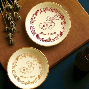 May include: Two small, round, white decorative plates with gold rims. One plate has a red floral design with two hearts and the text "March 9, 2026". The other plate has a gold floral design with the same text.