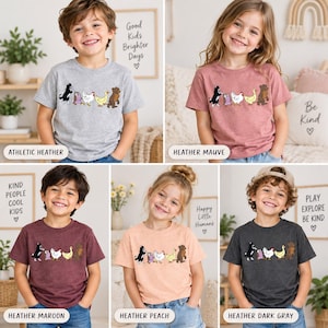 Op de afbeelding: Een collectie van vijf t-shirts met korte mouwen in athletic heather, heather mauve, heather maroon, heather peach en heather dark gray, elk voorzien van een grafische print van een hond, uil, kip, eend en beer die in een rij lopen.
