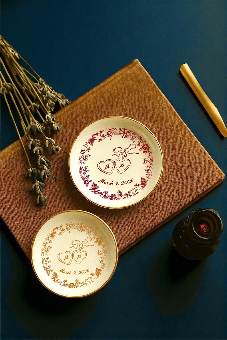 May include: Two small, round, white decorative plates with gold rims. One plate has a red floral design with two hearts and the text "March 9, 2026". The other plate has a gold floral design with the same text.
