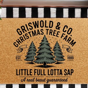 May include: A rectangular doormat with the text "GRISWOLD & CO. CHRISTMAS TREE FARM" and "LITTLE FULL LOTTA SAP". The design includes three green Christmas trees and the year "1989". The mat is brown with a black and white striped border.
