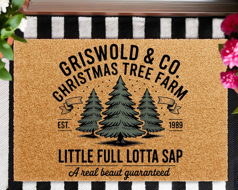 May include: A rectangular doormat with the text "GRISWOLD & CO. CHRISTMAS TREE FARM" and "LITTLE FULL LOTTA SAP". The design includes three green Christmas trees and the year "1989". The mat is brown with a black and white striped border.
