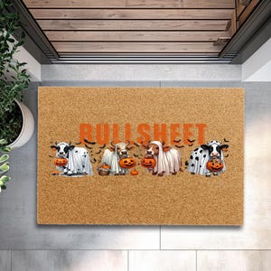 May include: A rectangular tan coir doormat featuring the orange text BULLSHEET above four illustrations of black and white cows wearing white ghost costumes and holding orange jack-o'-lantern buckets, surrounded by small black bats.
