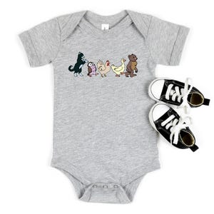 Op de afbeelding: Een grijs gem&ecirc;leerde babybody met korte mouwen en een grafische print van een zwart-witte kat, een kleine uil, een kip, een eend en een bruine beer die in een rij lopen, vergezeld door een paar zwart-witte canvas hoge sneakers.