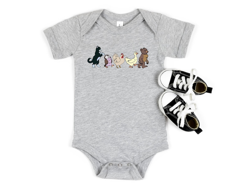 Op de afbeelding: Een grijs gem&ecirc;leerde babybody met korte mouwen en een grafische print van een zwart-witte kat, een kleine uil, een kip, een eend en een bruine beer die in een rij lopen, vergezeld door een paar zwart-witte canvas hoge sneakers.