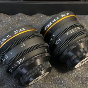 May include: Two black camera lenses with gold rings. The lens on the left is labeled "MIR-1V 37mm" and the lens on the right is labeled "HELIOS 44-2 58mm".
