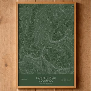 May include: A framed topographic map print of Handies Peak, Colorado, featuring white contour lines on a dark green background. The text reads Handies Peak, Colorado, San Juan Mountains, 14,058 ft, and coordinates 37 54 47 N 107 30 16 W.