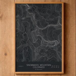 May include: A framed topographic map print of Snowmass Mountain, Colorado, featuring white contour lines on a black background. The text reads Snowmass Mountain, Colorado, 14,099 ft, and the coordinates 39 07 08 N 107 03 59 W in white.