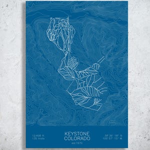 May include: A blue rectangular print featuring a white topographic map of Keystone, Colorado, with ski trail outlines. The text reads: KEYSTONE COLORADO, est 1970, 12,408 ft, 135 trails, and coordinates 39 36 18 N 105 57 15 W at the bottom.