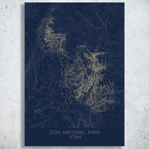 May include: A navy blue and gold topographic map print of Zion National Park, Utah. The map features detailed contour lines and the text "ZION NATIONAL PARK UTAH" at the bottom. The print is mounted on a white background.