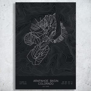 May include: A black poster featuring white topographic contour lines of Arapahoe Basin, Colorado. The text reads Arapahoe Basin, Colorado, est 1946, 13,050 ft, 147 trails, and coordinates 39 38 30 N 105 52 12 W. The design is minimalist and graphic.